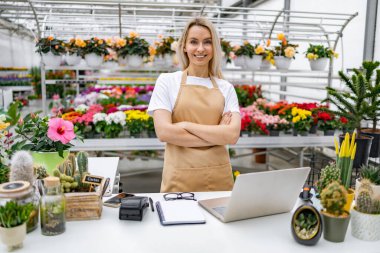 Gülümseyen beyaz bir kadın tezgahının önünde gururla durur. Etrafını güzel çiçekler ve bitkiler sarmış, satılmaya hazır..