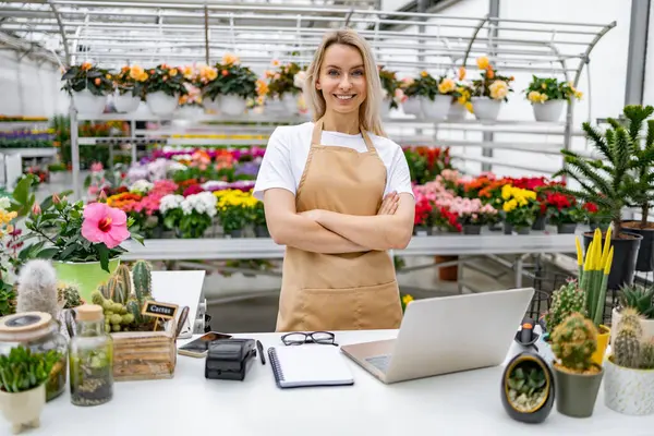Gülümseyen beyaz bir kadın tezgahının önünde gururla durur. Etrafını güzel çiçekler ve bitkiler sarmış, satılmaya hazır..