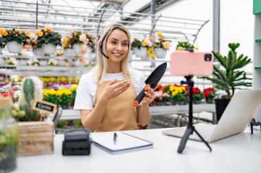 Bir çiçekçi dükkanında bahçe aletlerinin satışı için telefon kullanıyor. Bahçıvanlık tavsiyeleri ve ürün tanıtımı sunuyor..