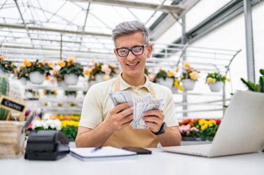 Çiçekçi dükkanındaki beyaz bir adam tezgahta nakit satışlarını memnuniyetle sayar..