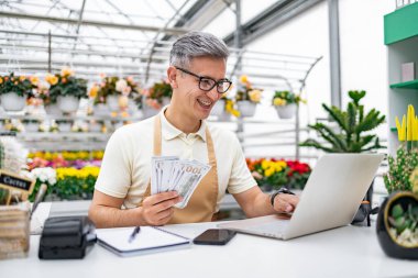 Beyaz bir adam, bir çiçekçi, dükkanındaki bir satış masasında başarıdan zevk alır, kazançlı bir günün ardından dizüstü bilgisayarla para sayar..