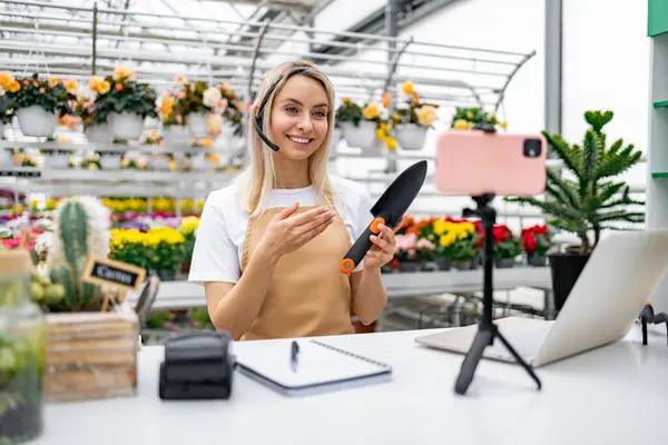 Bir çiçekçi dükkanında bahçe aletlerinin satışı için telefon kullanıyor. Bahçıvanlık tavsiyeleri ve ürün tanıtımı sunuyor..