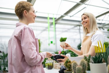 Bir müşteri çiçekçiden bir bitki satın alıyor. Çiçekçi, müşteri parasını öderken küçük bir fabrika işletiyor..
