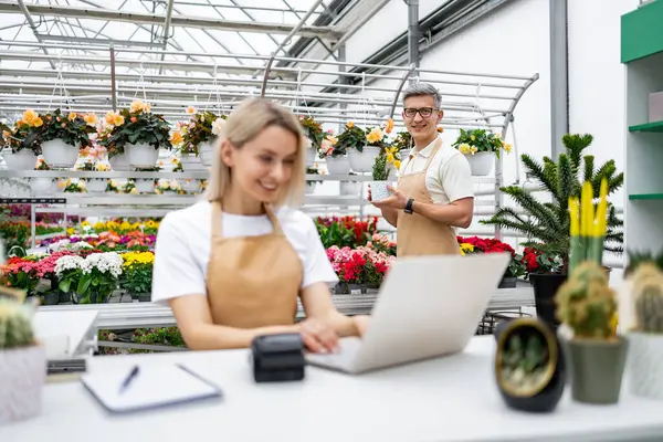 Kafkasyalı bir çiçekçi ve satıcı dükkanlarında çalışmaktan mutlu. Bitkiler arka planı doldurur ve bir adam saksı bitkisiyle poz verir..
