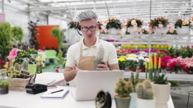 Kafkasyalı bir çiçekçi bir serada müşteriye online olarak yardım ediyor, bir video görüşmesinde kaktüs gösteriyor..