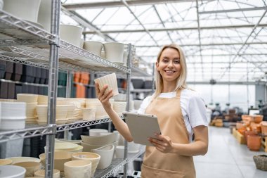 Kafkasyalı bir kadın fabrikada çalışıyor, gülümsüyor, elinde saksı ve tablet tutuyor..
