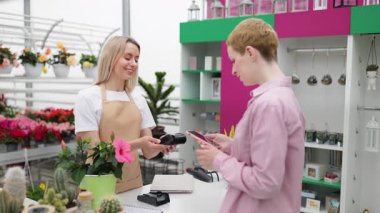 Bir müşteri çiçekçi dükkanından akıllı telefon kullanarak satın almak için ödeme yapıyor. Tezgahtar küçük bir bitki öneriyor..