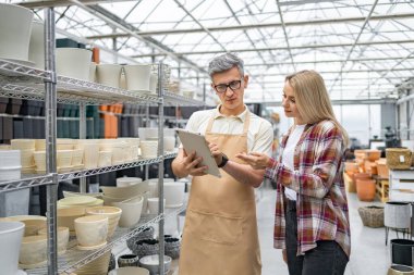 Bir çiçekçi, müşteriye dijital tablet kullanarak, çeşitli seramik saksılarla mükemmel saksıları seçmesinde yardımcı oluyor..