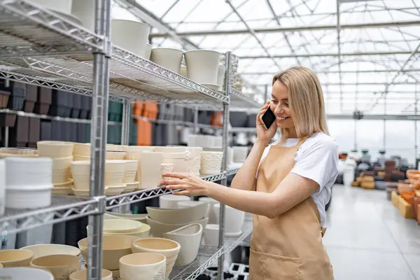 Dost canlısı bir tezgahtar, parlak bir dükkanda çeşitli saksılarla çevrili telefonuyla konuşur..