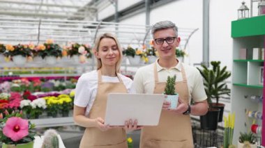 Dizüstü bilgisayarı ve saksı bitkisi olan mutlu çiçekçiler, bir sürü çiçekle dükkanda onaylarını veriyorlar..