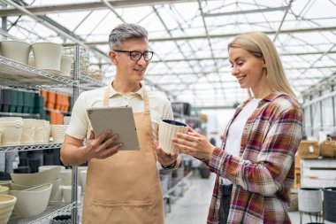 Kafkasyalı bir kadın, bir çiçekçide bir tezgahtarla birlikte, satın almak için nesneyi tartışıyor..