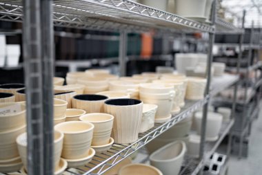 Çeşitli saksılarla dolu raflar bir fabrikada satılmaya hazır, farklı boyutlarda ve tasarımlarda sergileniyor..