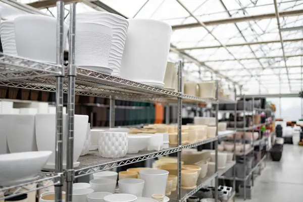 Bir fabrika dükkanının raflarında çeşitli şekil ve boyutlarda çiçek saksıları sergileniyor..