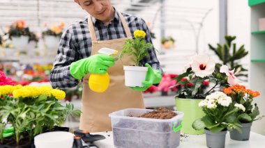 Bir bahçıvan, renkli çiçekler ve bahçe aletleriyle çevrili bir seradaki saksıyı sular..
