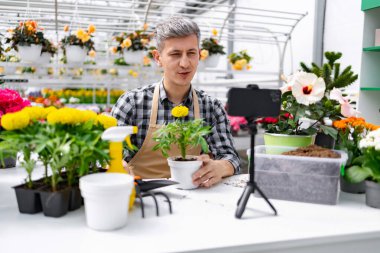 Serada bir adam bahçe teknikleri gösteriyor, bir saksı bitkisini elinde tutarak video kaydediyor..
