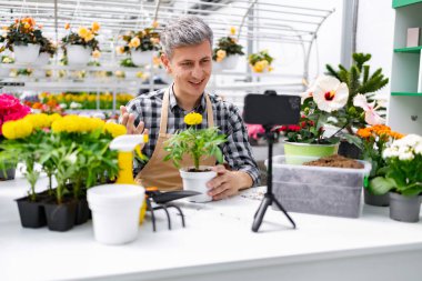 Seradaki bir adam bahçeyle ilgili bir video kaydediyor. Etrafı bitkiler ve çiçeklerle çevrili..