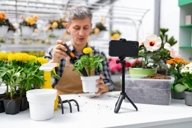 Önlüklü bir adam bitki ve çiçeklerle bahçe kursunu çekiyor..