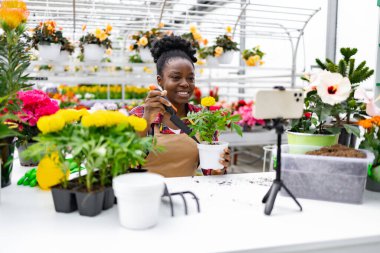 Afro-Amerikalı bir kadın, çiçeklerle bahçeyle ilgili bir dersi kaydederken gülümsüyor..