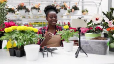Afro-Amerikalı bir kadın, çiçeklerle bahçeyle ilgili bir dersi kaydederken gülümsüyor..