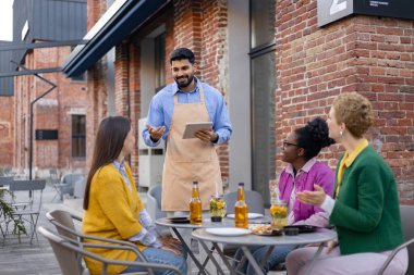 Bir garson, açık bir kafede oturan bir grup kadından tablet sipariş alır..