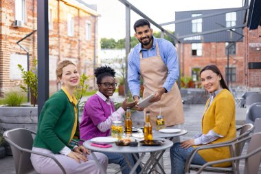 Dost canlısı bir garson, açık bir kafede oturan bir grup kadından sipariş alır..