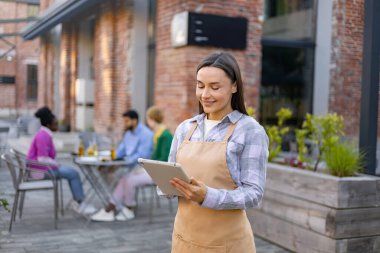 Gülümseyen bir garson açık hava restoranında tablet sipariş alıyor..