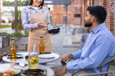 Bir bayan garson açık hava restoranındaki bir müşteriye ödeme terminali sunar..