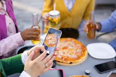 Arkadaşlarla dışarıdaki bir toplantıda pizza çekilirken telefonla çekilmiş yakın plan bir fotoğraf..