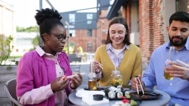 Çeşitli arkadaş grupları açık havada suşi yiyor, gülüyor ve sıradan bir öğle yemeği sırasında iyi vakit geçiriyor..