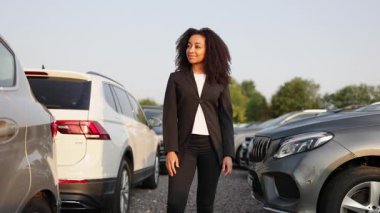Kendine güvenen takım elbiseli bir kadın arabaların yanında duruyor. Muhtemelen bir araba satıcısı ya da menajer..