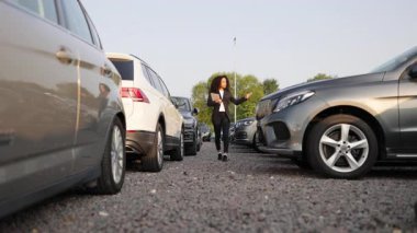 Araba galerisinde spor ceketli bir Afro-Amerikalı kadın. Etrafı farklı araba modelleriyle çevrili..