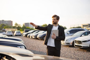 Bir araba satıcısı, güneşli bir günde potansiyel alıcılara özelliklerini vurgulayarak vitrindeki araçlara doğru hareket eder..