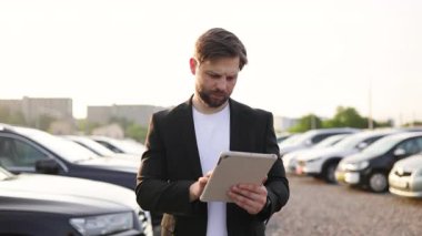 Bir araba satıcısı elinde tablet tutarken gülümser, arka planda otomotiv reklamı için mükemmel bir jest yapar..