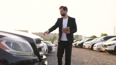 Bir araba satıcısı, güneşli bir günde potansiyel alıcılara özelliklerini vurgulayarak vitrindeki araçlara doğru hareket eder..