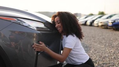 Bir kadın diz çöker, yeni bir arabaya sarılır, bir galeride neşe ve heyecan gösterir..