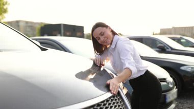 Gülümseyen bir kadın yeni bir arabaya bakıyor, kaputuna dokunuyor ve bir galeriden alışveriş yapmayı düşünüyor..