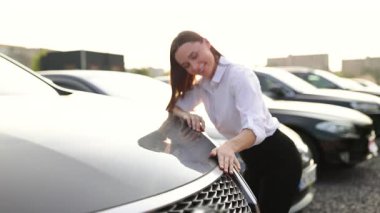 Bir kadın yeni bir arabanın kaputuna bakarken gülümsüyor..