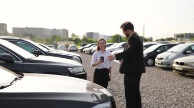 Erkek bir araba satıcısı araba galerisinde kadın bir müşteriyle seçenekleri tartışıyor..