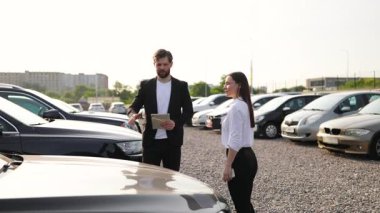 Bir erkek araba satıcısı, araba galerisindeki bir kadına bir aracı açıklar..