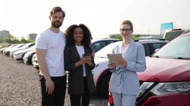 Bir araba galerisinde üç kişi kırmızı bir arabanın önünde müşteri memnuniyetini gösteriyor..