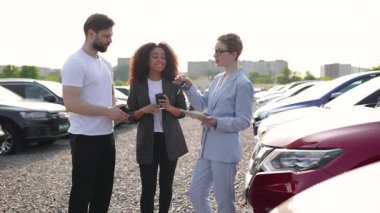 Bir araba satıcısı, parlak güneş ışığı altında bir galeriden yeni bir araç seçerken bir çifte yardım ediyor..