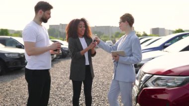 Mutlu bir siyah kadın yeni bir araba satın almayı kutluyor. Anahtarları ve kahve fincanını kaldırıyor. Arka planda bir araba satıcısı ve bir adam var..