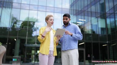 İki iş arkadaşı, modern bir ofis binasının dışında tablet kullanarak, işbirliği ve iletişimi vurgulayarak iş görüşmeleri yapıyorlar..
