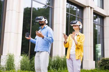 Binanın önünde VR kulaklıklar takan iki kişi huşu ifadeleriyle sanal gerçekliği deneyimliyor..