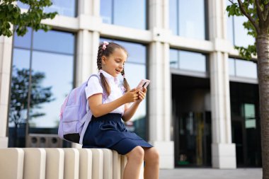 Okul binasının dışında akıllı telefon kullanan sırt çantalı kız öğrenci..