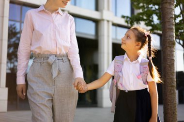 Bir anne ve ilkokul öğrencisi kızı okul bahçesinde el ele tutuşuyorlar..