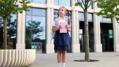 Gülümseyen bir liseli kız elinde bir kitapla ve sırt çantasıyla eğitime hazır bekliyor..