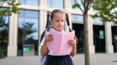 Okul bahçesinde elinde pembe bir kitapla örülü bir kız öğrenci, öğrenmeye hazır..