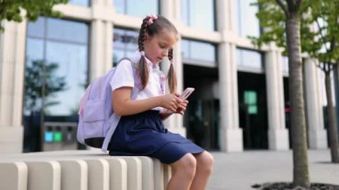 Okul ortamında cep telefonu kullanan at kuyruklu genç bir kız sırt çantası taşıyor..