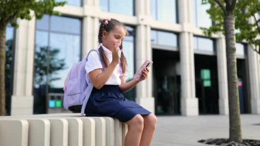 Genç liseli kız telefonuna el sallayarak binanın önündeki duvarda oturuyor..